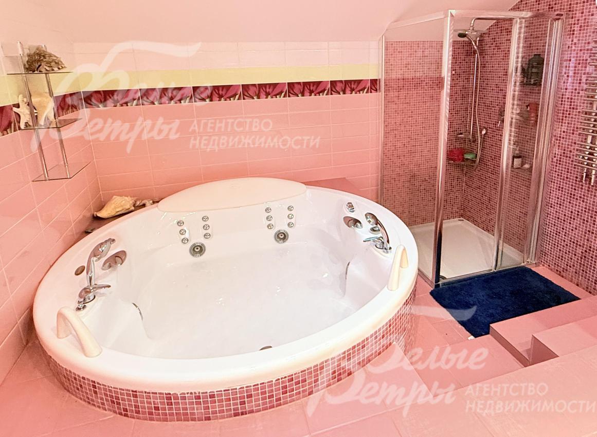 Ванна установлена на приподнятом основании, облицованном мелкой мозаичной плиткой розового оттенка, рядом - душевая кабина