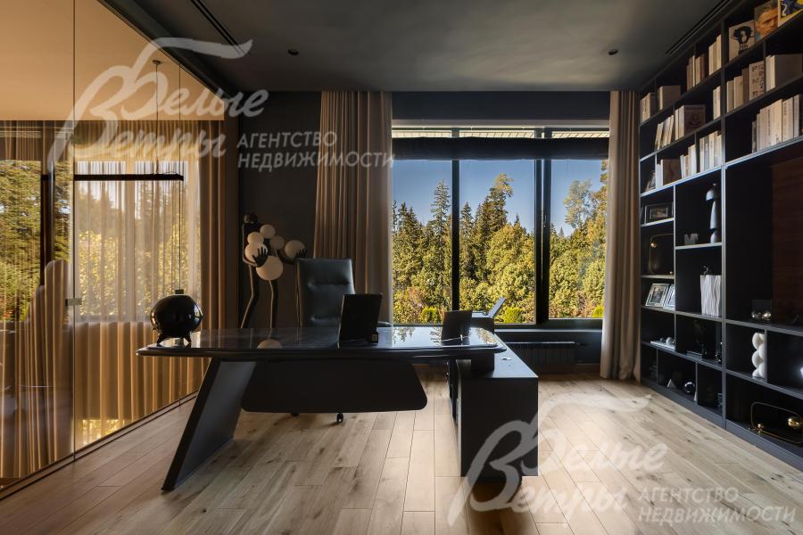 В кабинете с панорамными окнами установлено рабочее место и стеллаж для книг и документов