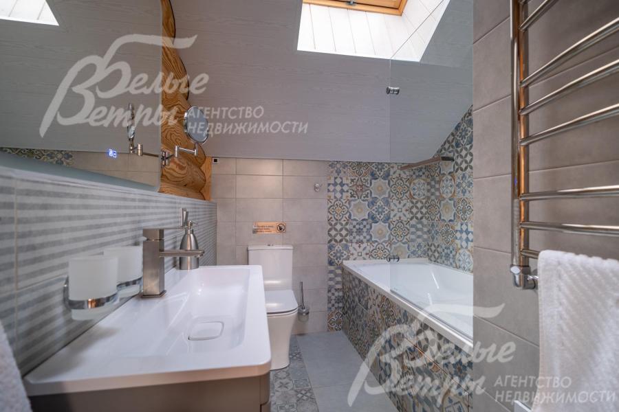 Общий санузел на втором этаже - с ванной, оформлен гладкой плиткой светлого оттенка, зона вокруг ванны выделена декоративной плиткой с орнаментом