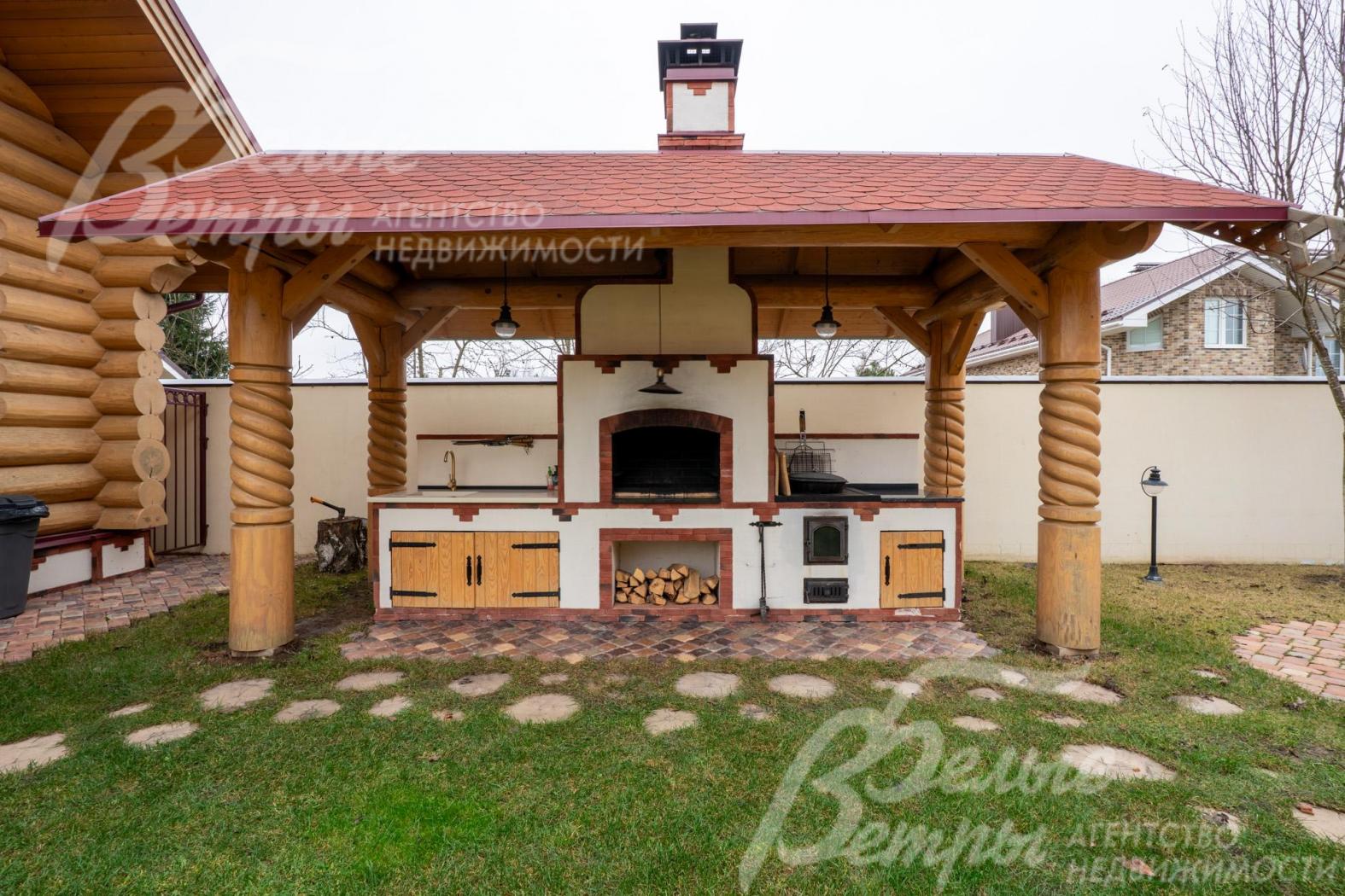 На участке - уличная кухня с крытым блоком в стилистике русской печи, интегрированной в деревянную беседку