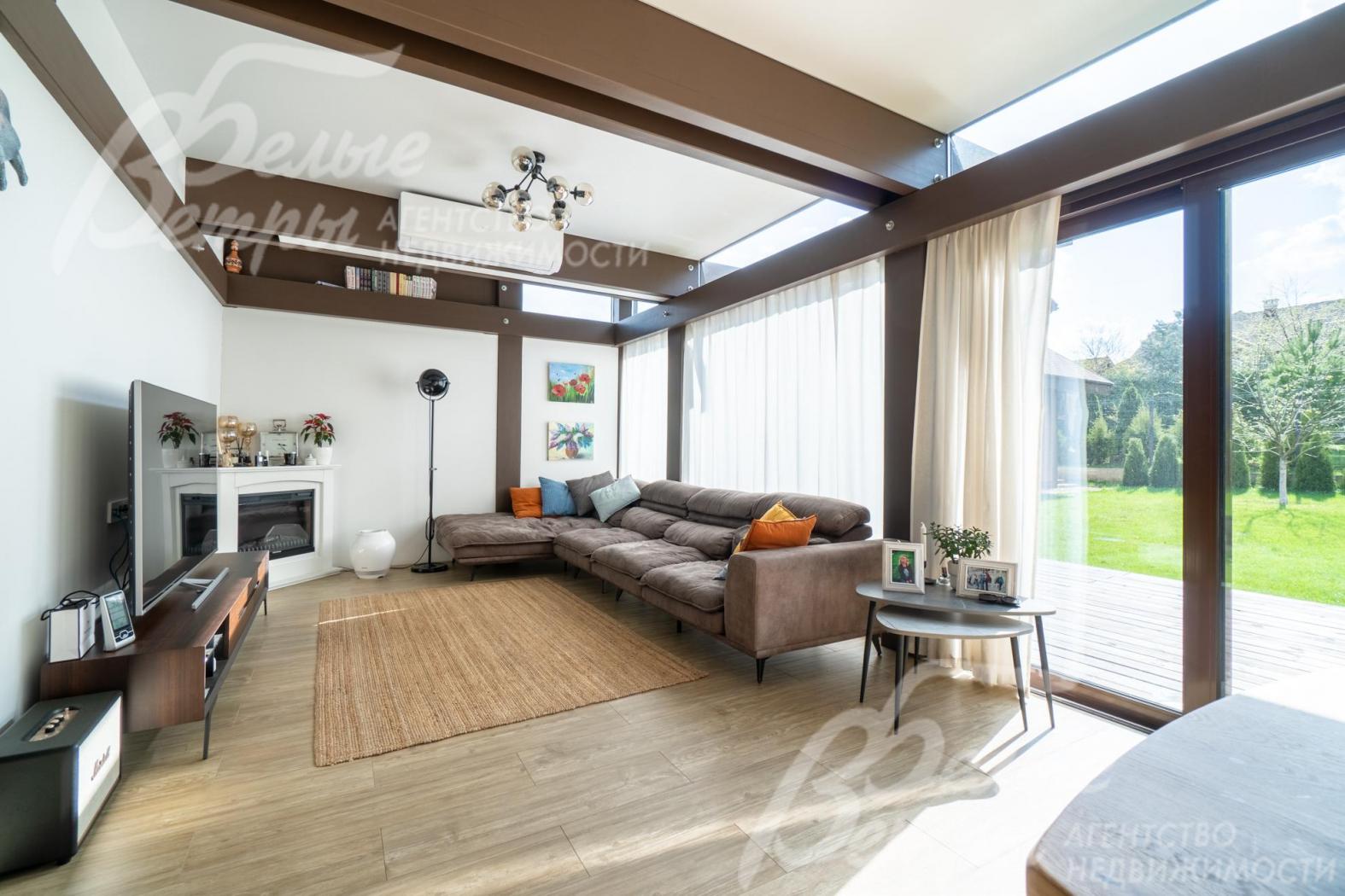 Гостиная максимально наполнена светом за счёт панорамного остекления, интерьер украшают массивные контрастные балки и электрический камин