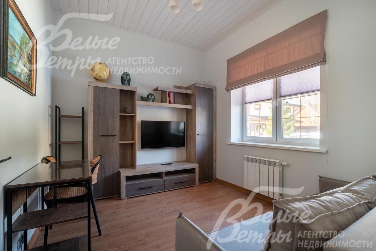 Одна из спален в основном доме расположена на первом этаже, в спальне - стенка с ТВ, диван и рабочий стол