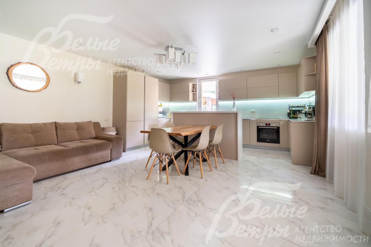 Просторная кухня-гостиная на первом этаже: установлен кухонный гарнитур с островом, обеденный стол из карагача