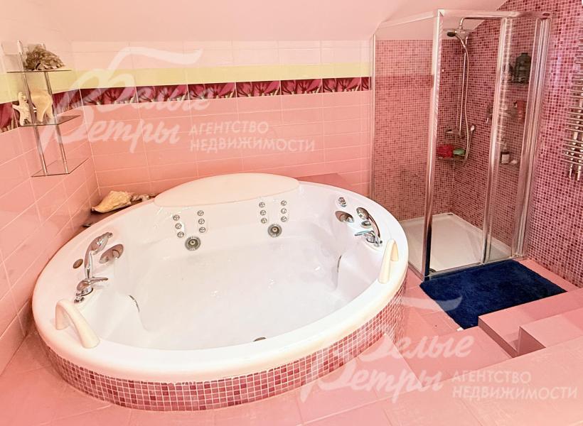 Ванна установлена на приподнятом основании, облицованном мелкой мозаичной плиткой розового оттенка, рядом - душевая кабина