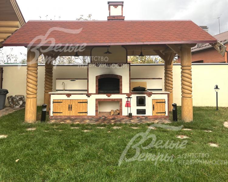 На участке - уличная кухня с крытым блоком в стилистике русской печи, интегрированной в деревянную беседку