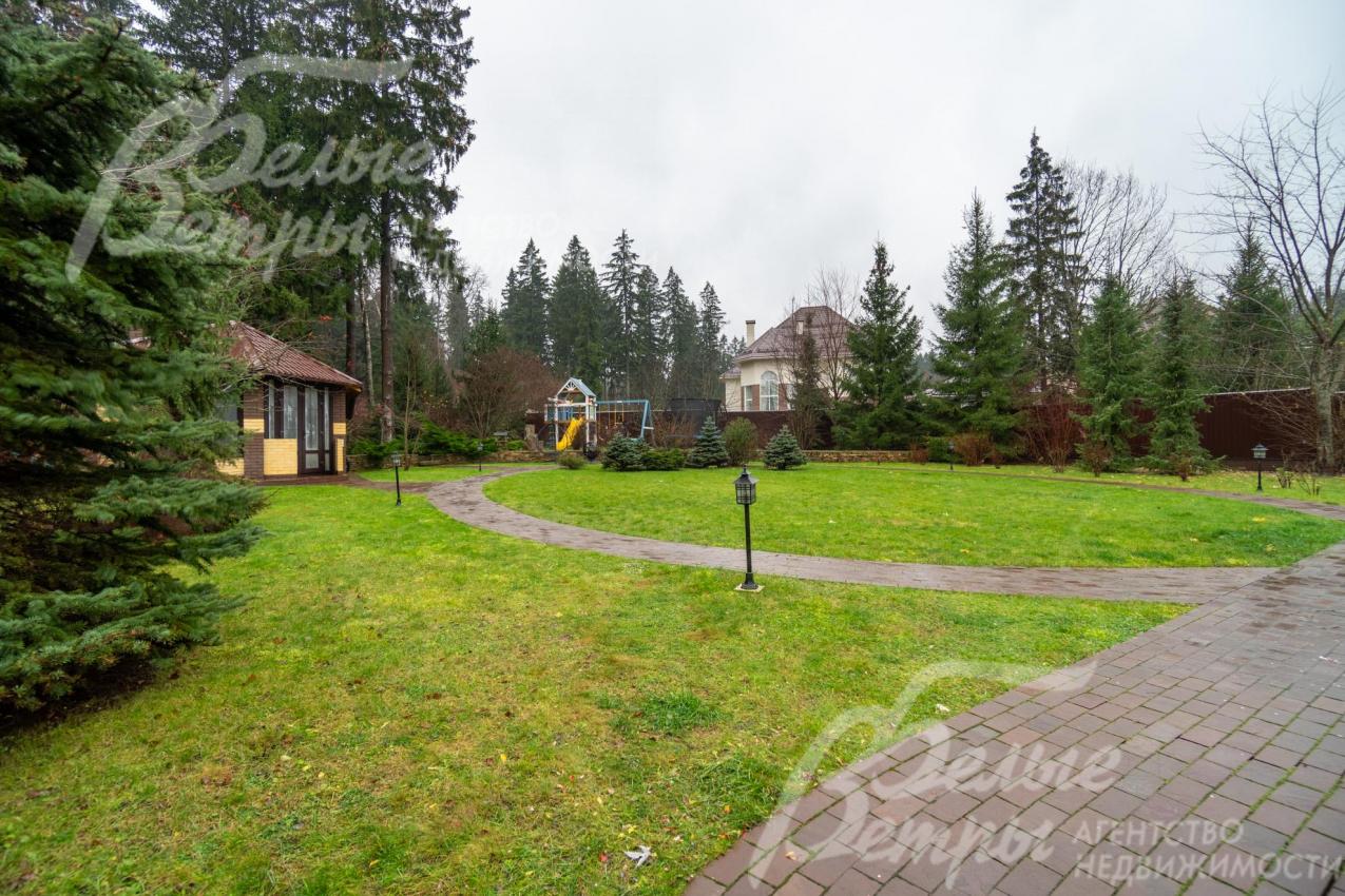 На участке – ровный рельеф с газонным покрытием, проложены дорожки с подсветкой, вдоль них стоят фонари